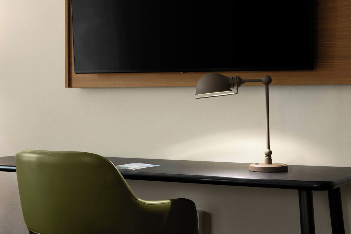 Ett modernt rum med ett skrivbord, en stol, en lampa och en platt-TV som är monterad på väggen.