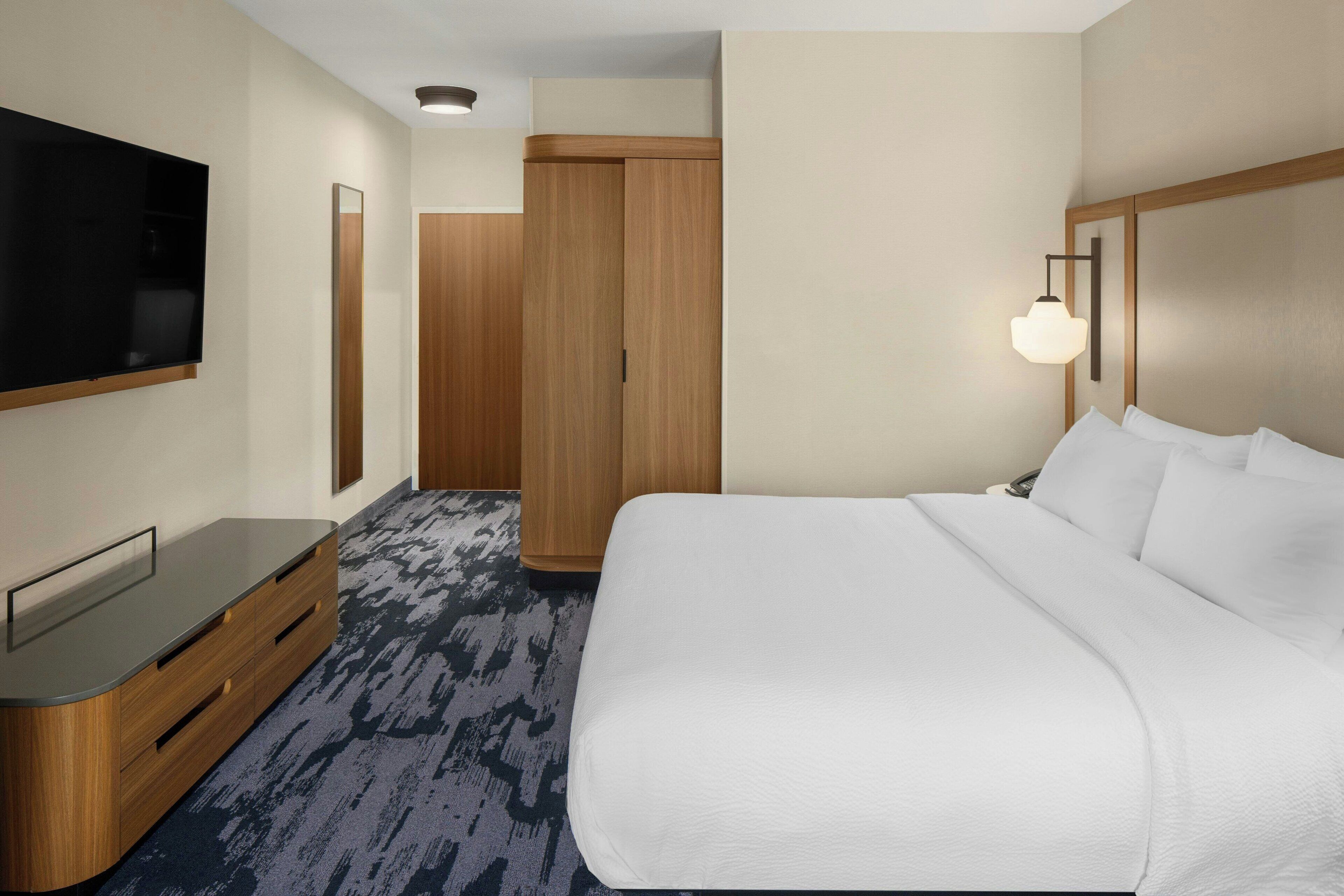 Ein Hotelzimmer mit einem großen Bett, einem flachbildfernseher an der Wand, einem Holzschrank und einem Teppichboden.