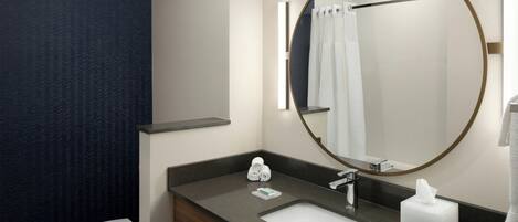 A modern bathroom with a dark blue patterned wall, a white toilet, a dark countertop sink, a mirror with a gold frame, and a towel rack.