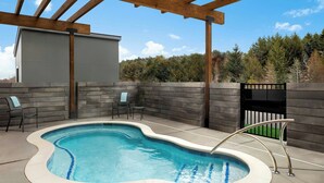 A swimming pool with a wooden pergola overhead, surrounded by stone walls and a view of trees. - Fairfield by Marriott Inn & Suites Traverse City (Traverse City)
