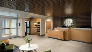 A modern hotel lobby with a reception desk, a seating area with a round table, and a snack bar. - Fairfield by Marriott Inn & Suites Traverse City (Traverse City)