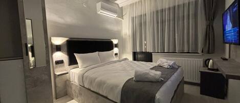 A modern hotel room with a bed, a desk, a television, and an air conditioning unit.
