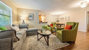 Una sala de estar con sofá, sillones, una mesa de centro y una zona de comedor al fondo.