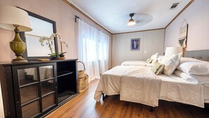 Un dormitorio con cama, mesita de noche, lámpara, espejo y ventana con cortinas.