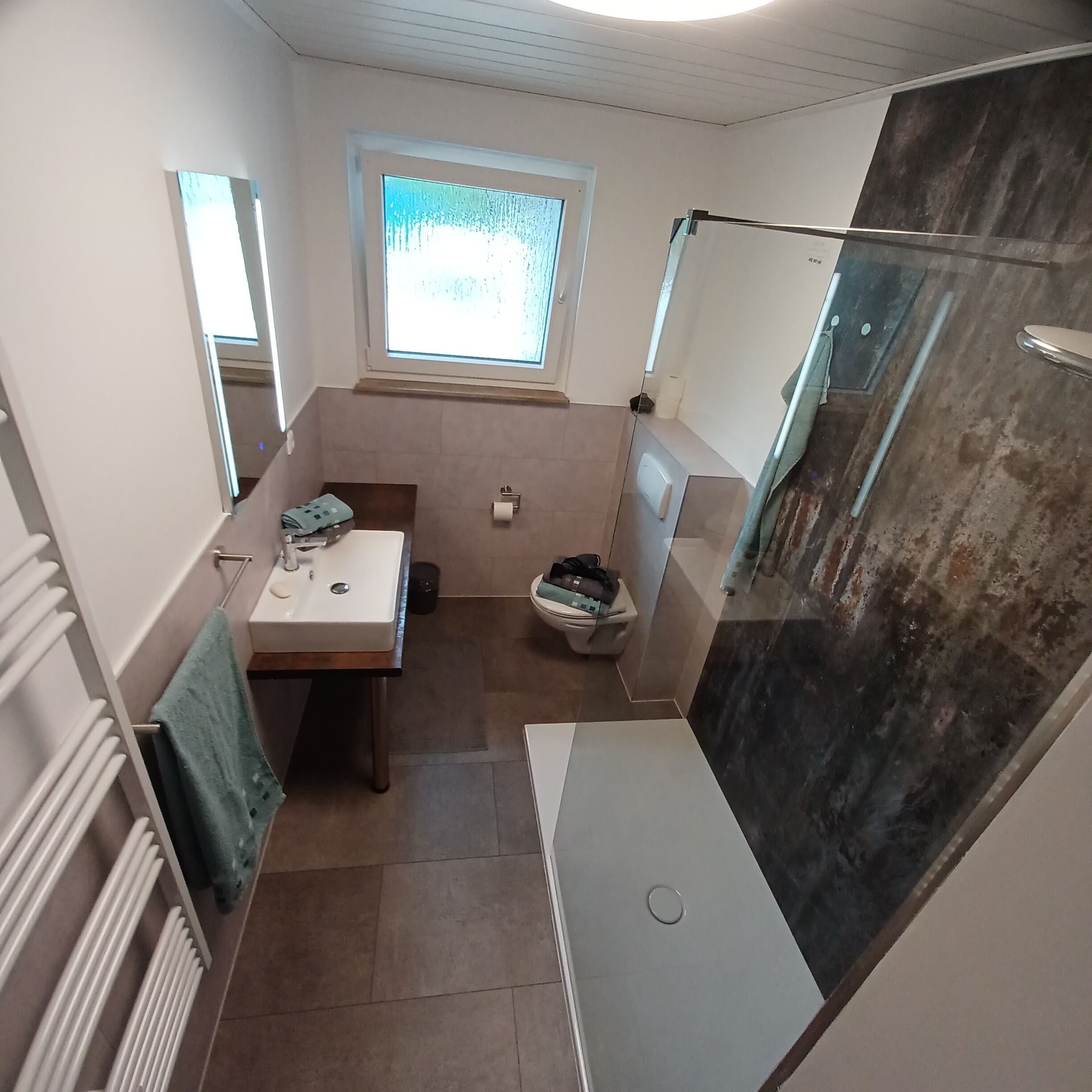 A bathroom with a sink, toilet, and shower. There is a window providing natural light and a towel rack.
