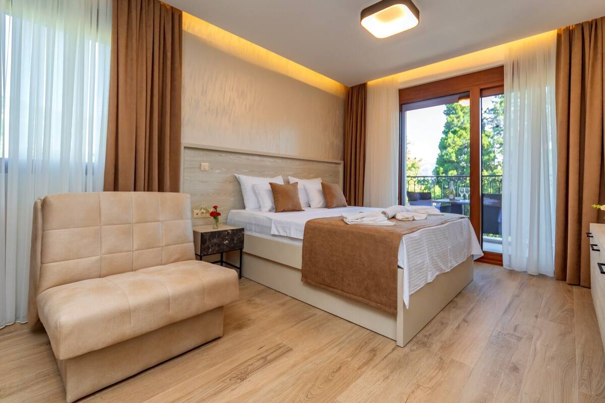 A modern hotel room with a large bed, a sofa, and a balcony with a view.