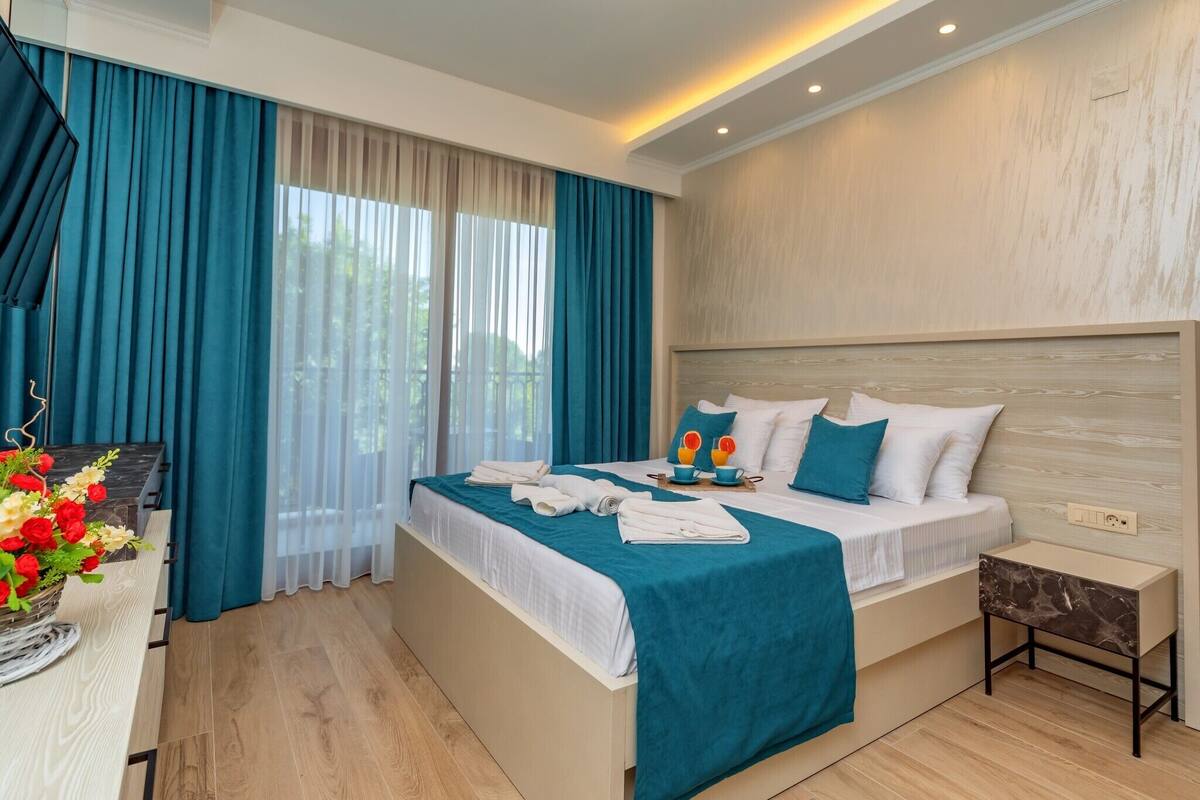 A modern hotel room with a large bed, a bedside table, and a view of the outdoors.