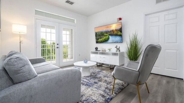 Ein modernes Wohnzimmer mit einem grauen Sofa, einem weißen Couchtisch und einem grauen Sessel. Ein weißes Sideboard beherbergt Dekorationselemente und an der Wand ist ein großer Fernseher angebracht.