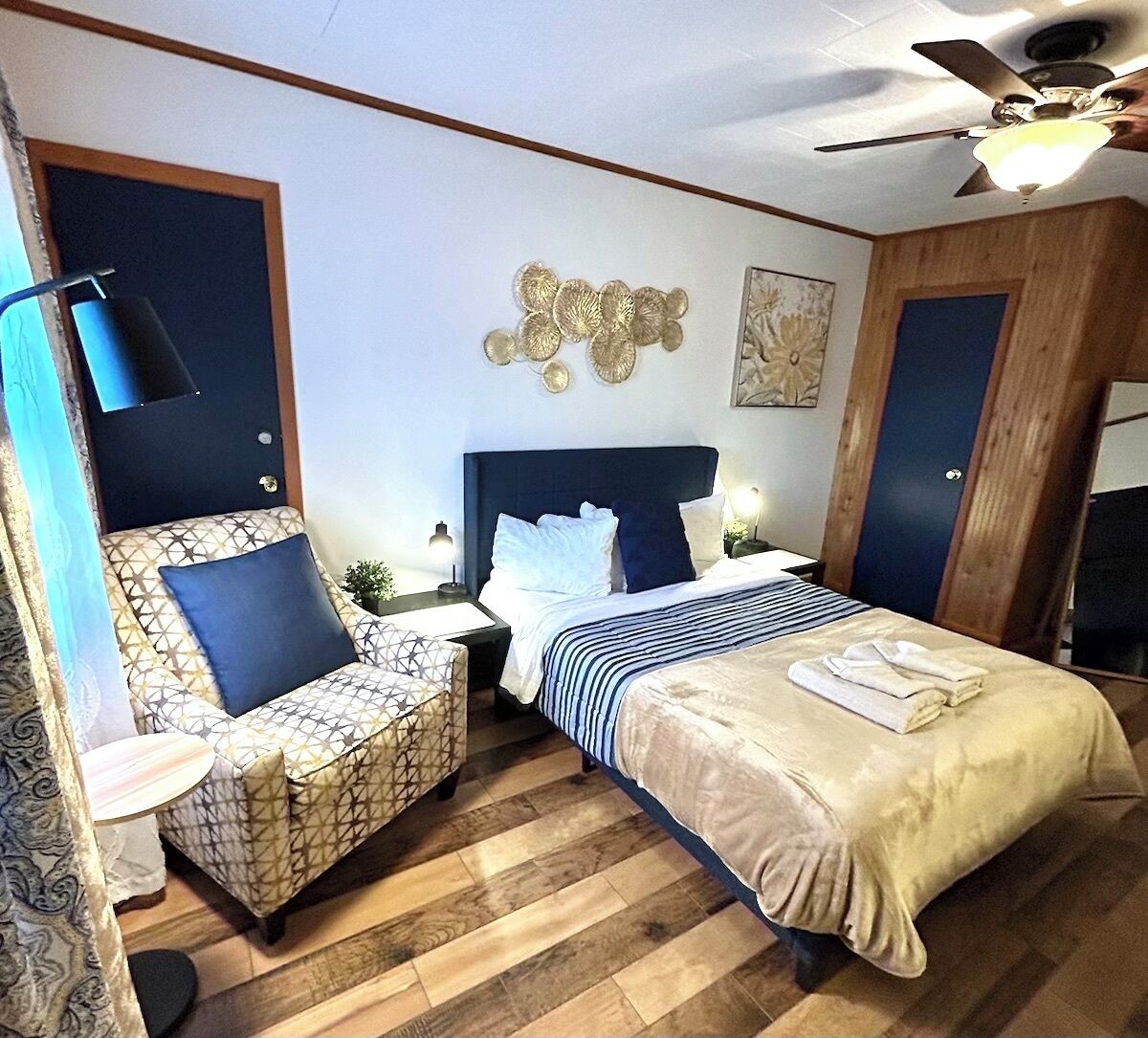 A bedroom with a large bed, two bedside tables, a ceiling fan, and a wall-mounted artwork.