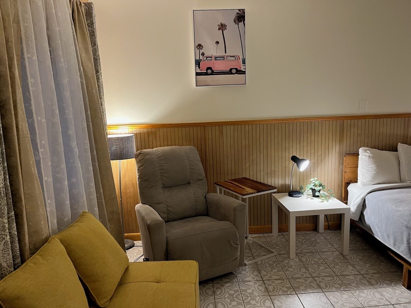 A hotel room with a bed, a small table with a lamp, a sofa, and a chair.