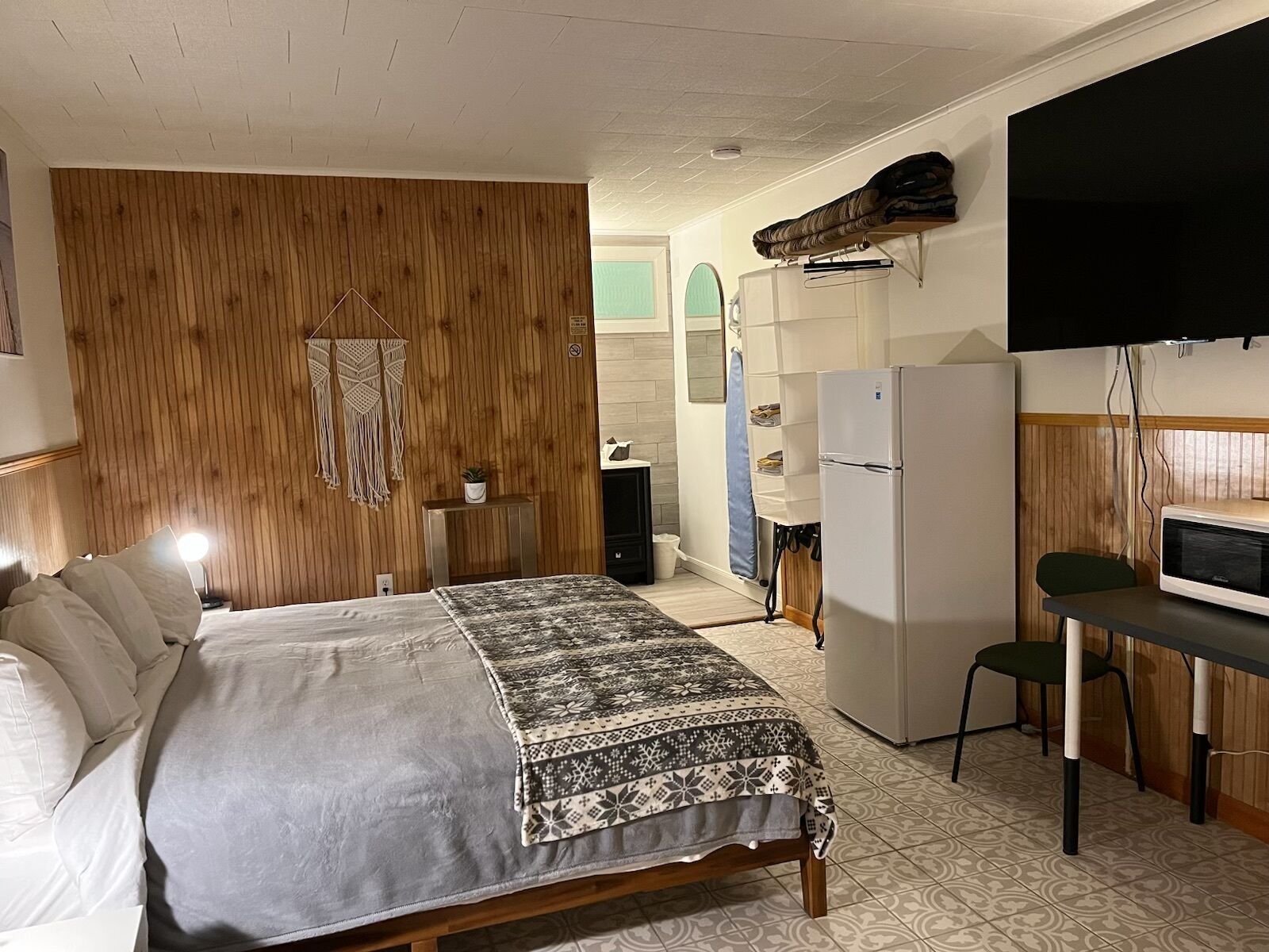 Una habitación pequeña con cama, escritorio, refrigerador y televisión.