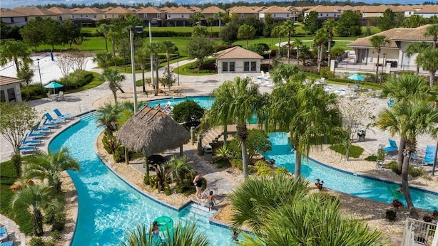 A resort with a large swimming pool, lounge chairs, and palm trees.