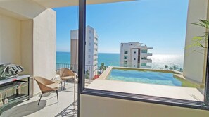 Ein Balkon mit Meerblick, ein Pool und ein Essbereich mit Stühlen und Tisch.