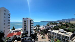 Ein Hotel an der Küste mit mehreren Etagen, Blick auf den Strand und einem Berg im Hintergrund.