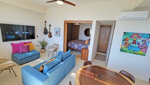 A modern living room with a blue sofa, a dining table, and a TV displaying a content selection screen.