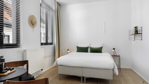 A modern bedroom with a large bed, a bedside table, a chair, and a window with blinds. - The 1880 Boutique Holiday Home in The Heart of Antwerp (Antwerpen)