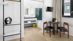 A modern bathroom with a shower, sink, and a TV mounted on the wall. There is a small table with chairs and a fan on a shelf. - The 1880 Boutique Holiday Home in The Heart of Antwerp (Antwerpen)