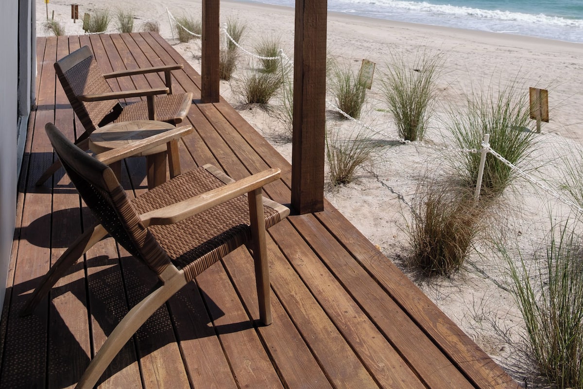 Een houten terras met een tafel en stoelen, met uitzicht op een strand.
