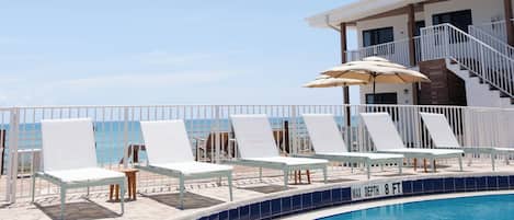 A pool area with lounge chairs and a staircase leading to an upper level.