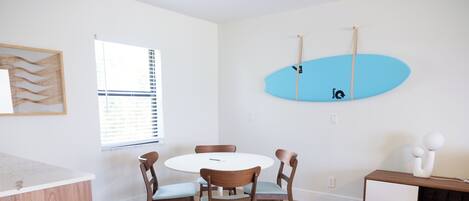 Un comedor con una mesa redonda y sillas, una tabla de surf en la pared y un armario con tapa blanca.