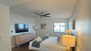 A bedroom with a bed, a ceiling fan, a TV, a dresser, and a window.