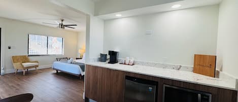 A modern kitchen with a dishwasher, microwave, and coffee maker. There is a dining table with a menu and a chair. The room has wooden flooring and a ceiling fan.