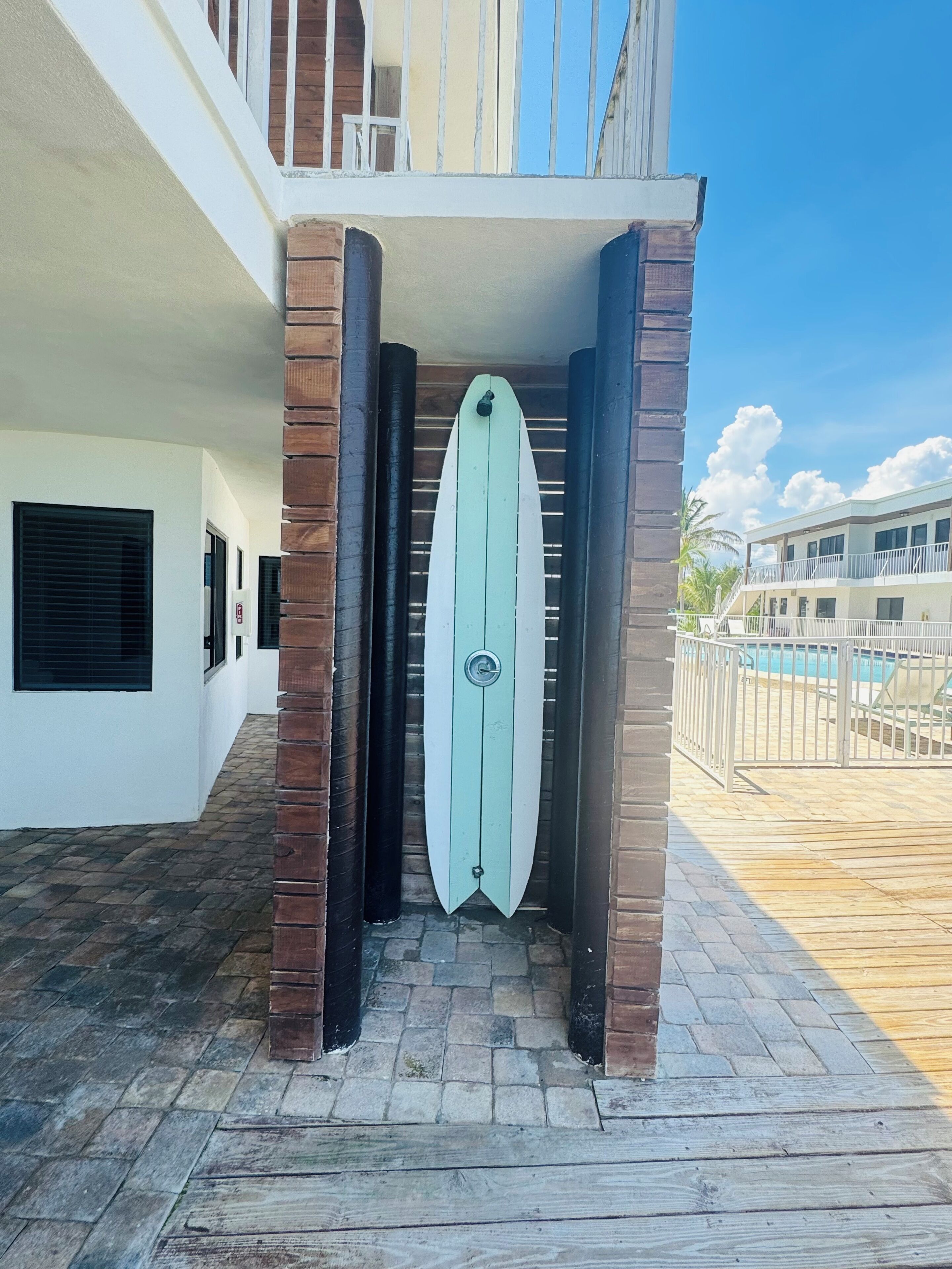 A building entrance with a surfboard-shaped door, brick pillars, and a pool area visible in the background.