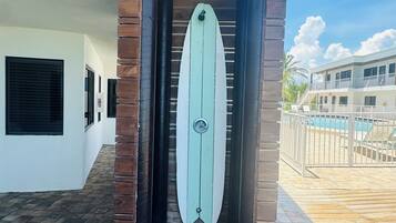 Entrada de edificio con puerta en forma de tabla de surf, pilares de ladrillo y una piscina visible al fondo.