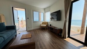 A modern living room with a wooden floor, a blue sofa, a wooden coffee table, and a view of the beach through large windows. - Melbourne Beach Resort & Surf Club  (Melbourne Beach)