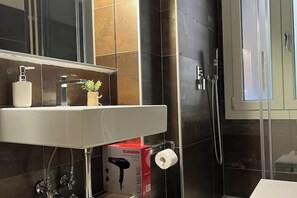 A bathroom with a white sink, a mirror, a hairdryer, and a shower.