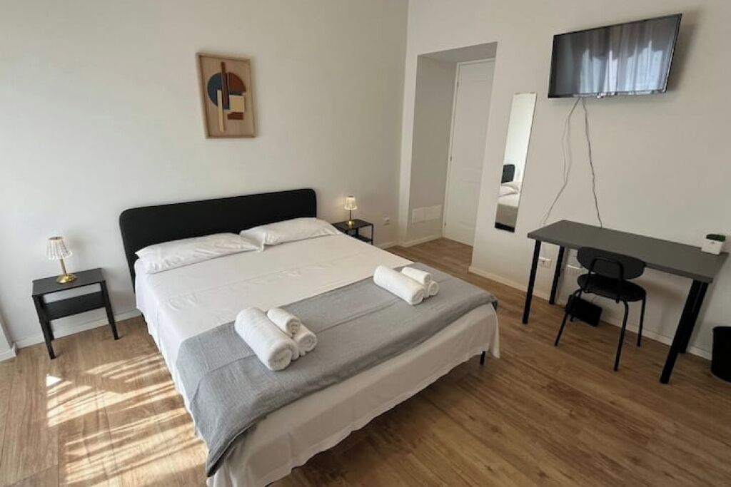Una camera d'albergo con un letto grande, una scrivania, una sedia, una TV e un tavolino con una lampada.