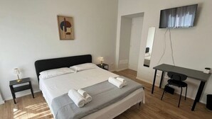 A hotel room with a large bed, a desk, a chair, a TV, and a small table with a lamp. - PiazzaBolognaStay - beautiful home in Rome (Roma)