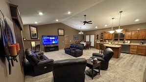 A spacious living room with a flat-screen TV, leather sofas, a dining area, and a kitchen. - Huge Breathtaking Cabin on Shetek/Swim-Grill-Games (Slayton)