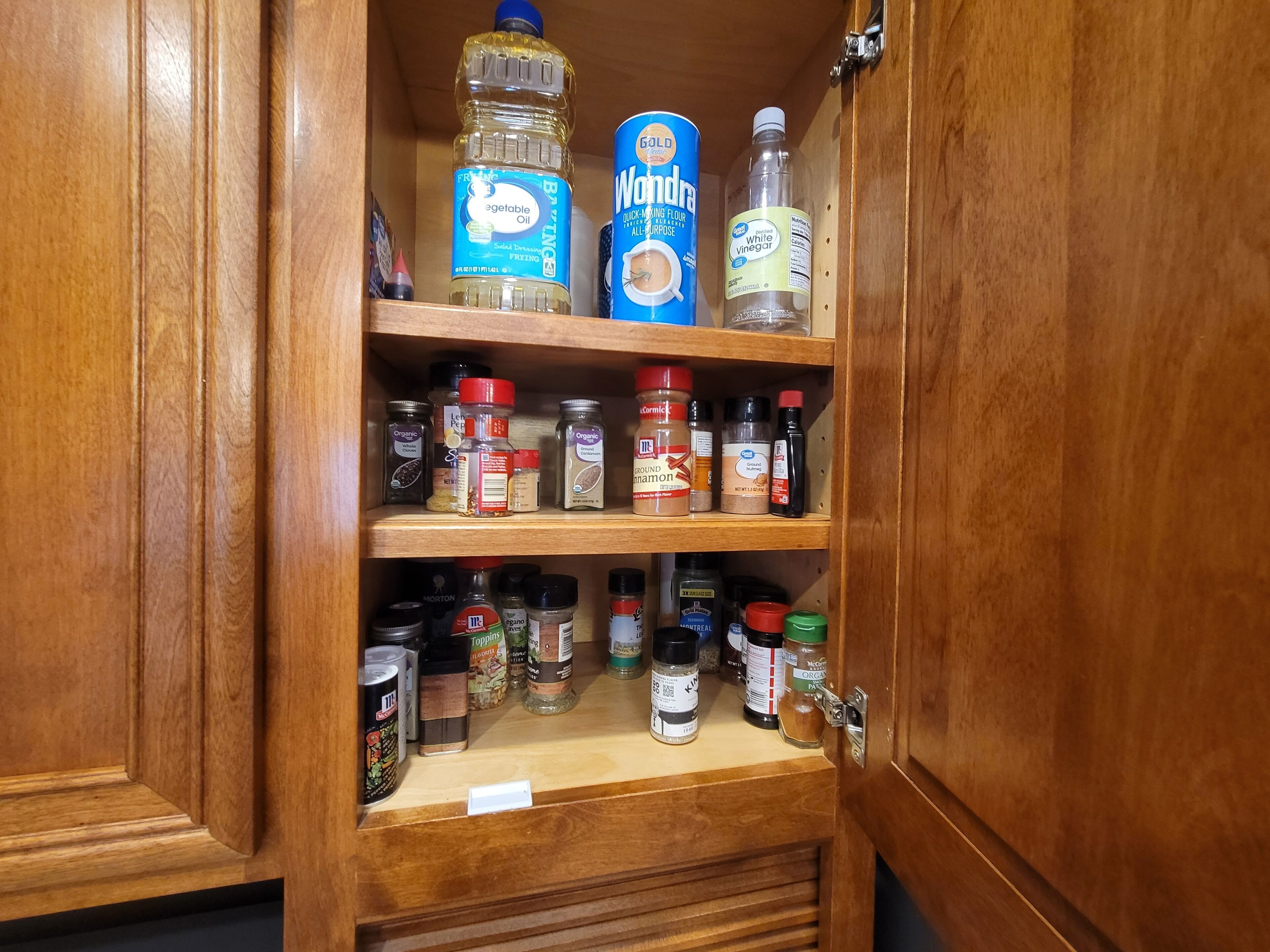 A wooden cabinet with multiple shelves containing various kitchen items such as bottles, jars, and containers.