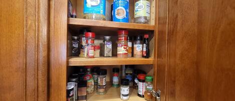 A wooden cabinet with multiple shelves containing various kitchen items such as bottles, jars, and containers.