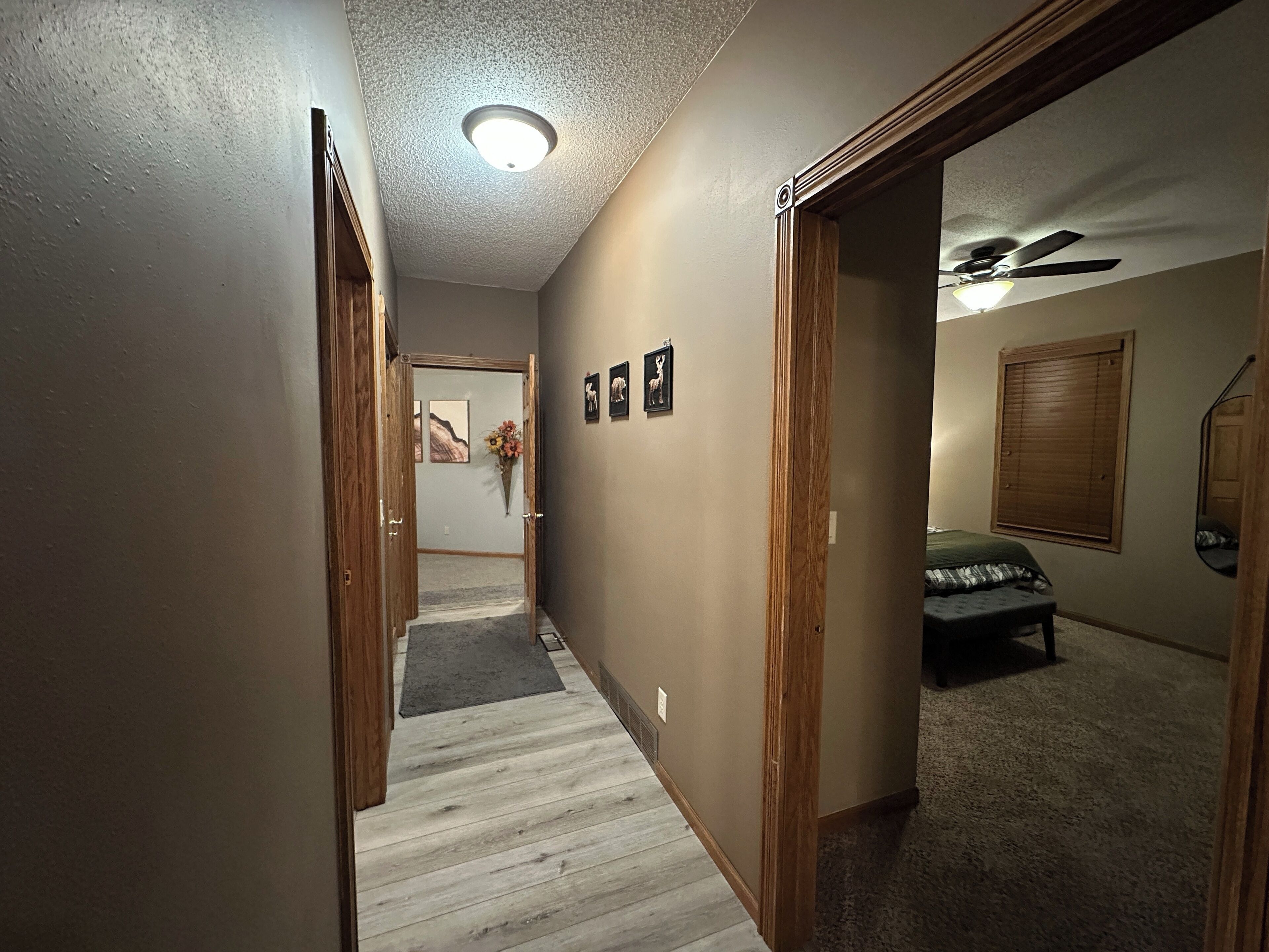 Un couloir avec un plancher en bois, un ventilateur de plafond et un lit dans la pièce adjacente.