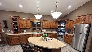 A modern kitchen with wooden cabinets, stainless steel appliances, and a central island with two chairs. - Huge Breathtaking Cabin on Shetek/Swim-Grill-Games (Slayton)