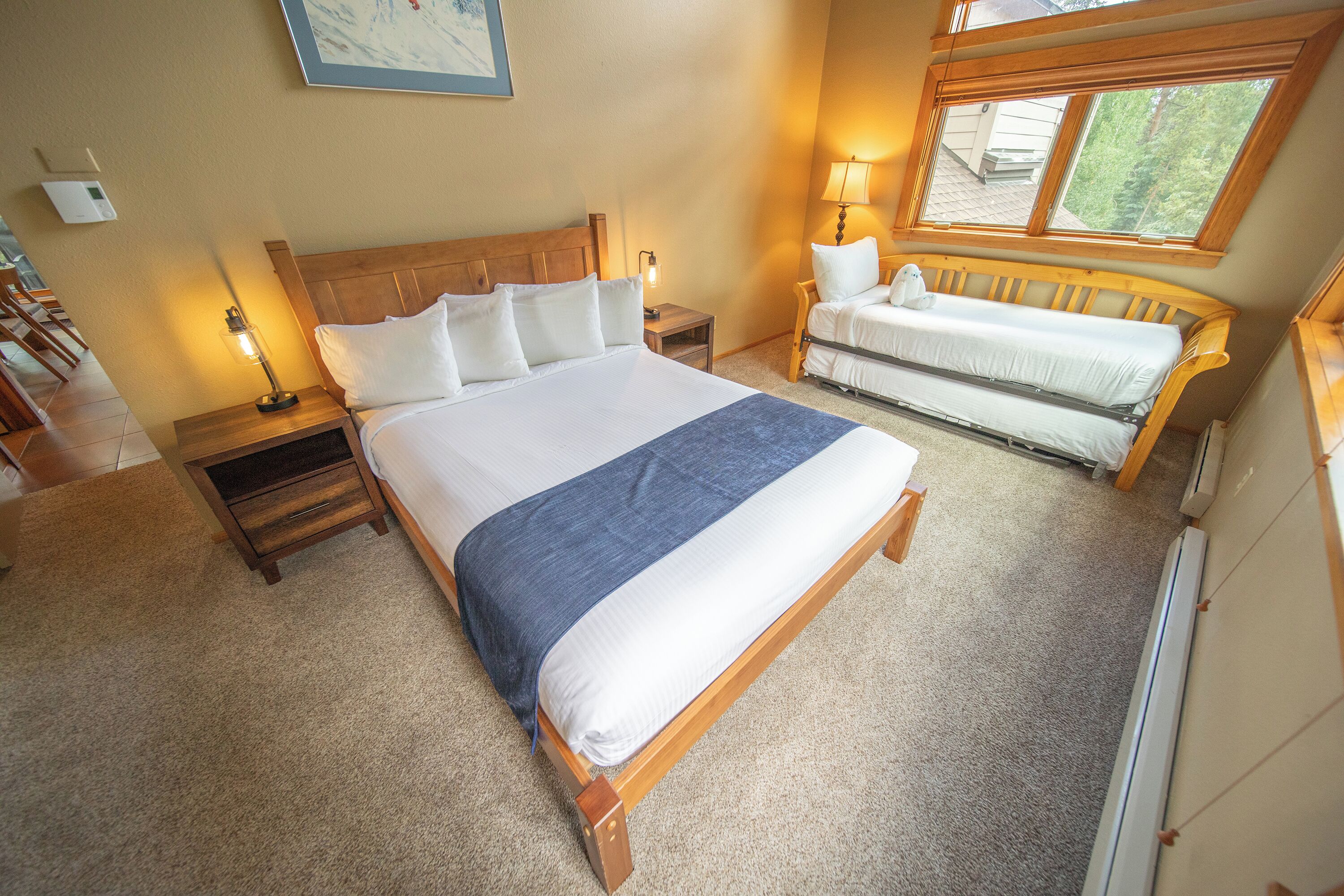A bedroom with a large bed, a bench, a nightstand, and a window with a view of trees.