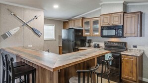 Une cuisine avec des meubles de rangement en bois, un réfrigérateur, un four à micro-ondes, une cuisinière et deux tabourets de bar.
