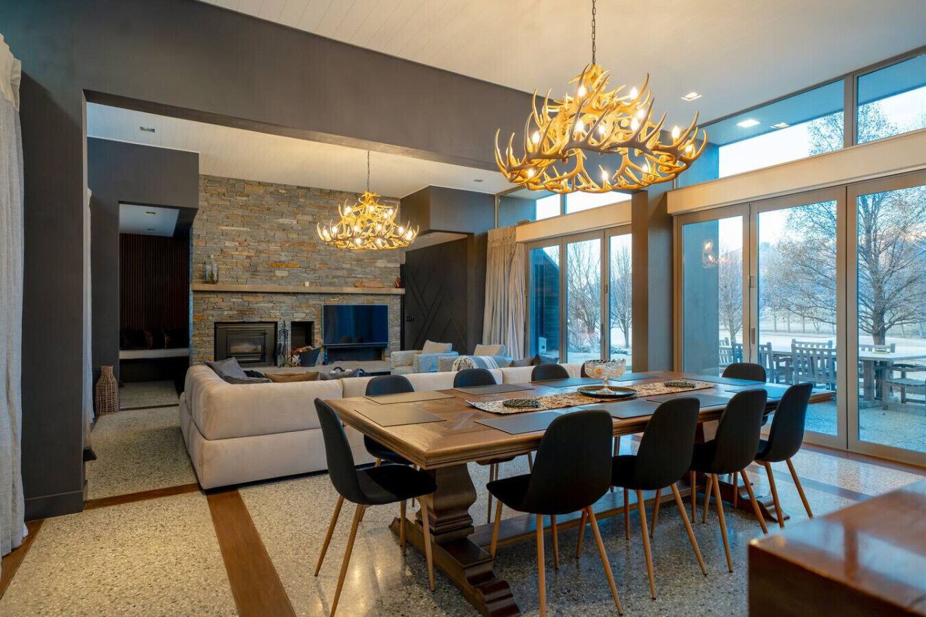 A modern dining area with a large table and chairs, a fireplace, and a stone wall.