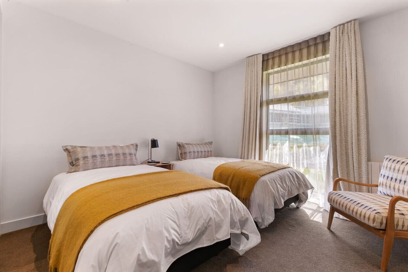 Habitación de hotel con dos camas, una silla y un ventanal grande con cortinas.