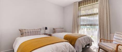 Habitación de hotel con dos camas, una silla y un ventanal grande con cortinas.