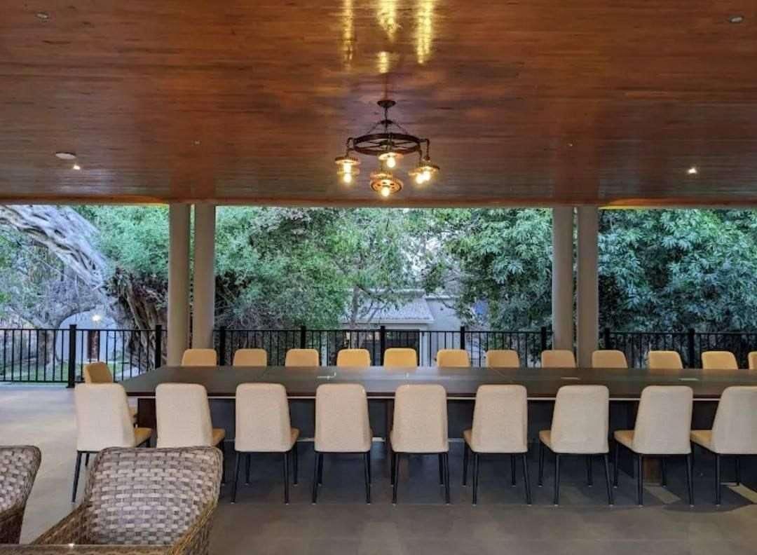Un espace de restauration intérieur avec une longue table et des chaises, un plafond en bois et une vue sur les arbres à l’extérieur.