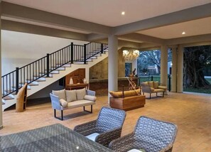 A spacious living area with a staircase, wicker furniture, and a fireplace. - Waters Edge By Serendib (Liwonde)