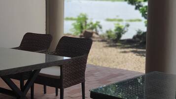 Un patio con mobili in vimini e un tavolo in vetro, affacciato su uno specchio d'acqua e del verde.
