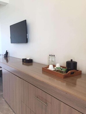 A hotel room with a wooden counter, a flat-screen TV mounted on the wall, a tray with toiletries, and a cabinet with drawers. - Waters Edge By Serendib (Liwonde)