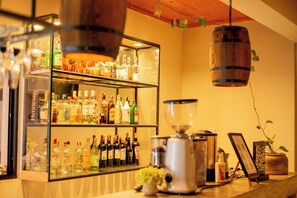 Eine Barbereich mit einer Auswahl an Spirituosenflaschen, einer Kaffeemaschine und einer hängenden Leuchte.