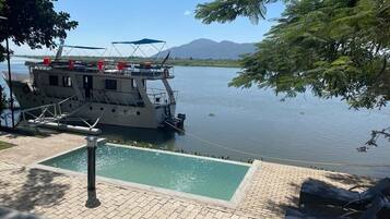 Un bote atracado junto a un lago tranquilo con una piscina pequeña y sillones de descanso.