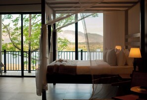 A bedroom with a bed, bedside lamps, and a view of a beach and mountains through large windows. - Waters Edge By Serendib (Liwonde)
