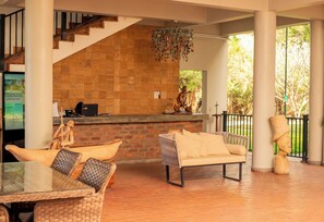 A lobby with a brick wall, a staircase, a reception desk, wicker furniture, and a hanging chandelier. - Waters Edge By Serendib (Liwonde)